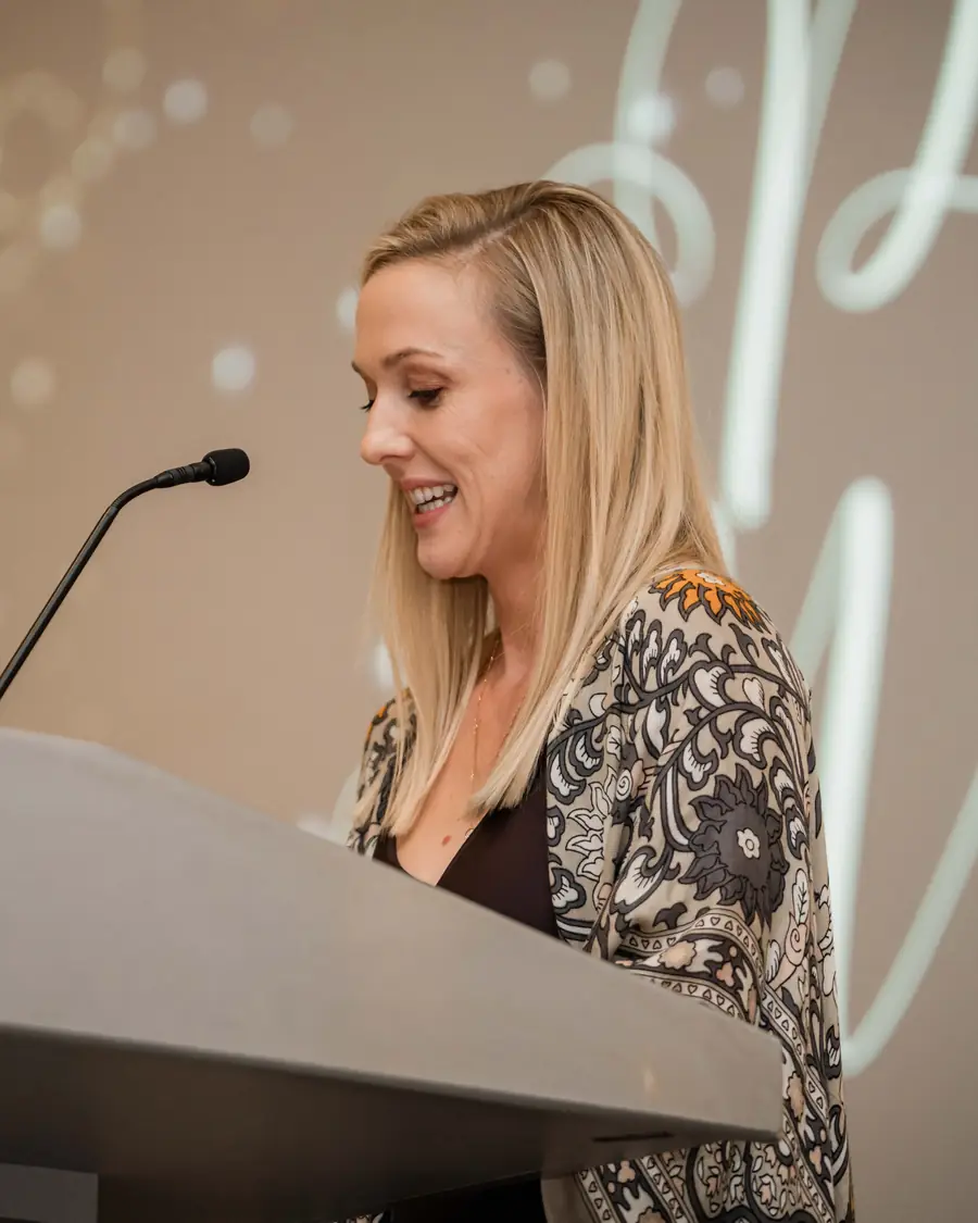 Sinéad Scully speaking at a lectern, smiling as she reads from her notes